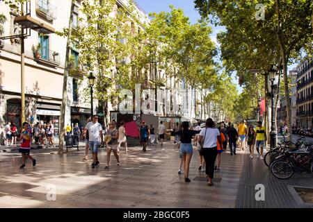 View of people walking, traditional and historical buildings and trees on famous street called 'La Rambla' in Barcelona. Stock Photo