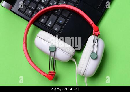 Electronics isolated on light green background, top view. Music and digital equipment concept. Headphones and black laptop. Earphones made of plastic with computer. Sound recording idea. Stock Photo