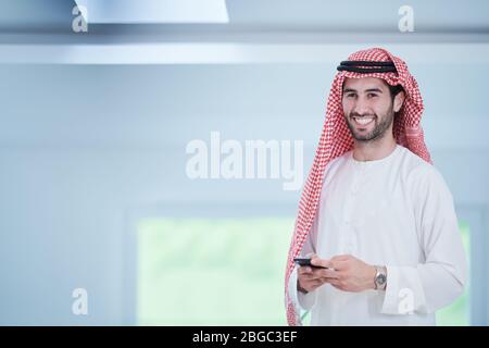 young modern muslim arabian businessman wearing traditional clothes while using smartphone at home Stock Photo