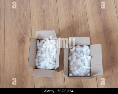Two cardboard boxes with packing foam pellets top view, on wooden floor. Stock Photo
