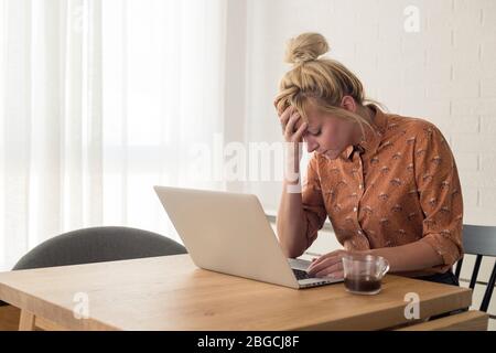 Young woman disappointed while working on laptop. He is sitting at table at home. Stock Photo