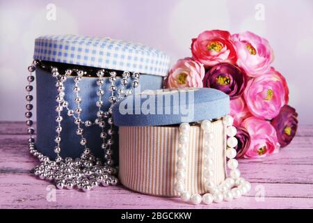 Decorative boxes with beads and flowers on table on bright background Stock Photo