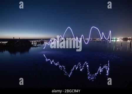 Amazing laser fireshow performance in the night blue sky with reflections in the sea water Stock Photo