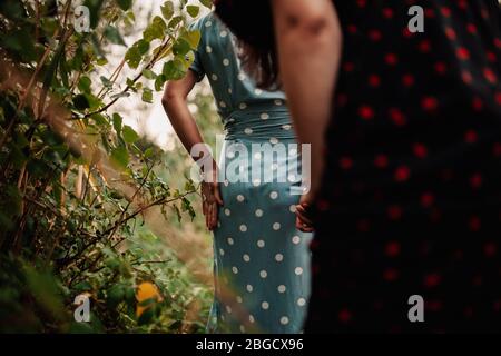 Back view of two young women walking through the field wearing dresses and sneakers Stock Photo