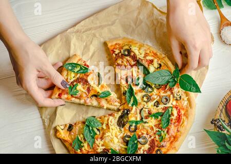 Hands taking slices of pizza. Hand holding slice pizza. Hand taking pizza slices from white wooden background Stock Photo