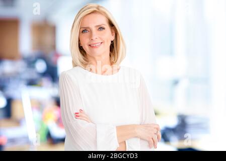 Close-up portrait of beautiful blond businesswoman standing in the office while looking at camera and smiling. Stock Photo