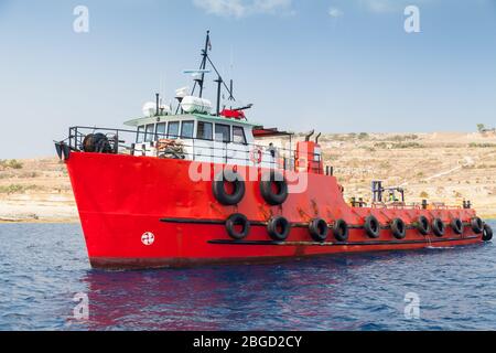 Tug boat with bright red hull goes near  Malta island at sunny day Stock Photo