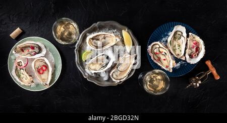 Oysters with various toppings panorama, shot from above with wine, with lemon and lime, pepper, onion, on a dark background Stock Photo