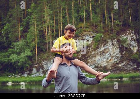 Father and son are smiling while spending time together. Little boy sits on father neck