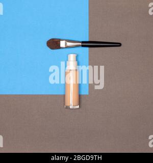 Makeup foundation bottle with make-up brush on blue and brown background, flat lay Stock Photo