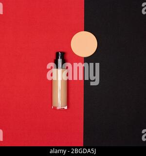 Makeup foundation bottle with makeup sponge on red and black background flatlay Stock Photo