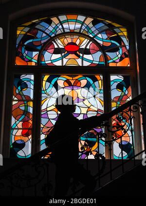 21 April 2020, Brandenburg, Frankfurt (Oder): An employee of the European University Viadrina can be seen in a staircase in front of a lead glass window by the Berlin artist D. Schölzel from 1980. Even though the summer semester has already begun, the university and the library will remain closed for the time being. Students from 107 countries are registered for the summer semester 2020 - this is a record at the European University Viadrina Frankfurt (Oder). The proportion of foreign students is also at a consistently high level: At 25 percent, this is twice as high as the national average (tw Stock Photo