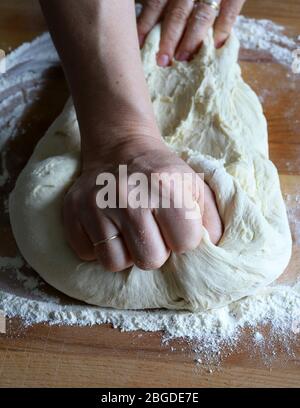 Cooking concept. Female hands preparing fresh homemade pizza dough on floured wooden board. Closeup. Italian cuisine. Stock Photo