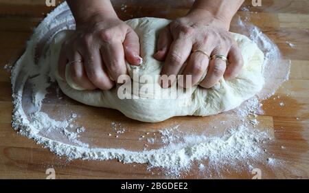 Cooking concept. Female hands preparing fresh homemade pizza dough on floured wooden board. Closeup. Italian cuisine. Stock Photo