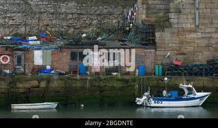 Old harbour of Seaham showing small inner harbour buildings along with lobster pots, marker flags and a small fishing boat