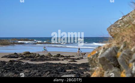 SUNNYSIDE BAY CULLEN MORAY FIRTH SCOTLAND TWO CYCLISTS AND A DOG ON THE SANDY BEACH Stock Photo