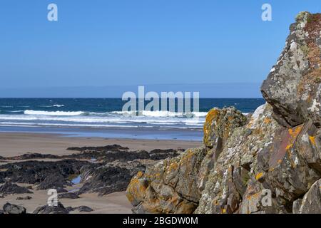 SUNNYSIDE BAY CULLEN MORAY FIRTH SCOTLAND YELLOW LICHENS ON ROCKS A BLUE SEA AND A SANDY BEACH Stock Photo