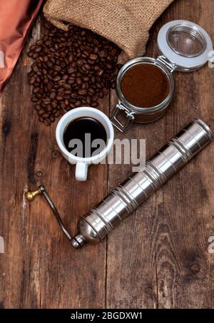 Bag of coffee on a wooden table. Coffee beans ground in a jar. Manual coffee grinder. Top view, place for text. Brown background. Packing coffee in a Stock Photo