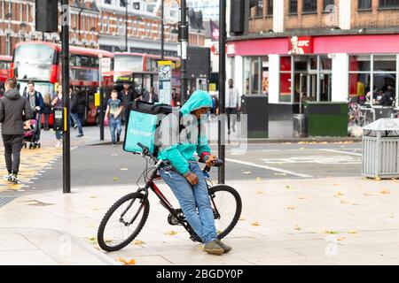 A deliveroo rider leaning on his bicycle and checking his phone in Windrush Square, Brixton, London Stock Photo