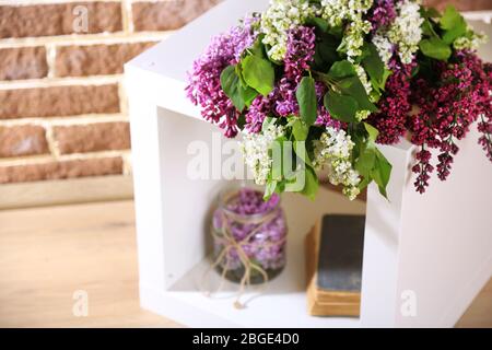 Beautiful lilac flowers in wicker basket, on stand, on color wall background Stock Photo