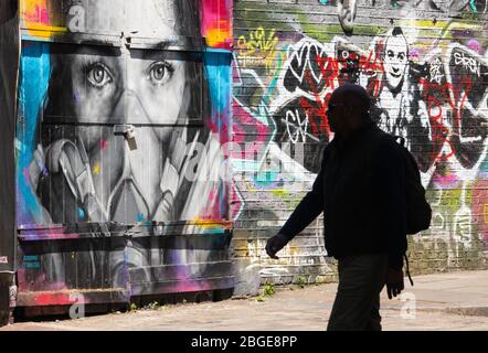 A man passes a mural showing a woman wearing a face mask, in Shoreditch, east London, as the UK continues in lockdown to help curb the spread of the coronavirus. Stock Photo