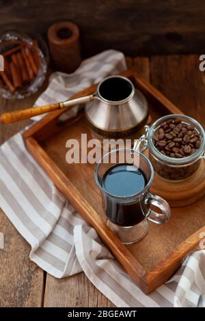 A cup of coffee on a wooden tray. Turk and coffee beans. Cook breakfast at home. Still life with a drink in a glass. Ground coffee, brew and prepare a Stock Photo