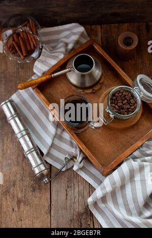 A cup of coffee on a wooden tray. Turk and coffee beans. Cook breakfast at home. Still life with a drink in a glass. Ground coffee, brew and prepare a Stock Photo