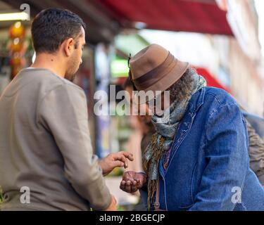 A man places a coin into the open hand of a woman on Electric Avenue, Brixton, London Stock Photo