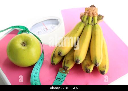 Bunch of mini bananas and measuring tape on scales, isolated on white Stock Photo