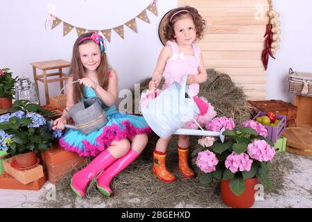 Beautiful small girls in petty skirts holding watering cans on country style background Stock Photo