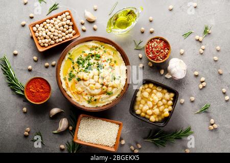 Hummus topped with chickpeas, olive oil and green coriander leaves on stone table with different spices aside. Flat lay Stock Photo