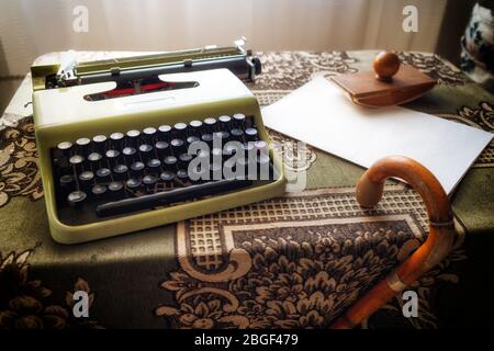 vintage desktop with an old typewriter, blank paper and a walking stick in the light of a nearby window Stock Photo