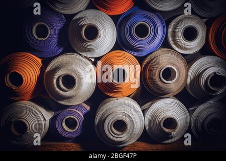 many textile rolls of blue, white and orange colors stacked one over the other in dark light Stock Photo