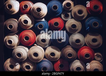 many textile rolls of blue, white and orange colors stacked one over the other in dark light Stock Photo
