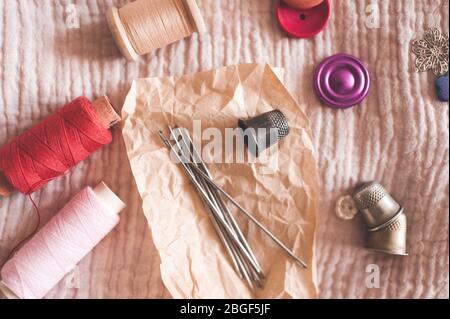 Thread spools with needles, buttons and thimbles on textile closeup. Top view. Handmade. Work at home. Stock Photo