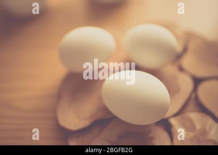 Three white chicken eggs on a wooden board and brown table. Stock Photo