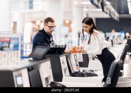 Side view of handsome man wearing glasses giving passport to staff at check in desk at airport Stock Photo