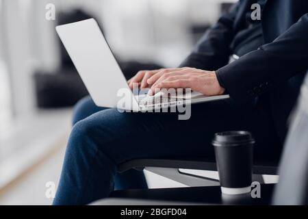 A business man sitting at the airport park working with his laptop and drinking takeaway coffee while waiting the flight departure. Stock Photo