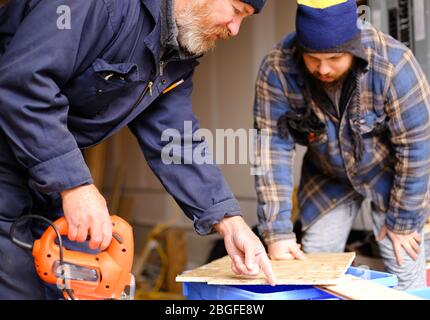 Handyman and apprentice cutting wood with jigsaw in workshop. Stock Photo