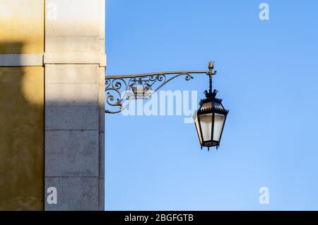 traditional street lamp lantern in Lisbon, Portugal, hanging from the wall of an historic yellow building with clear blue sky as background Stock Photo