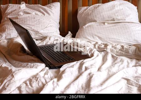 Laptop in unmade bed on background of grey crumpled sheets and pillows. Home office concept Stock Photo