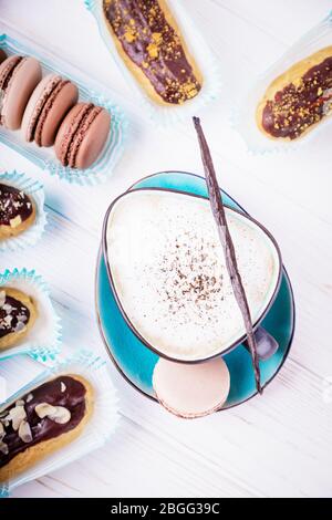 Cup of vanilla coffee cappuccino, chocolate macaroons and eclairs. Top view Stock Photo