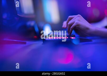 Hacker uses keyboard, shakes buttons with fingers to crack password. Internet security concept, cyber attack. Neon blue color Stock Photo