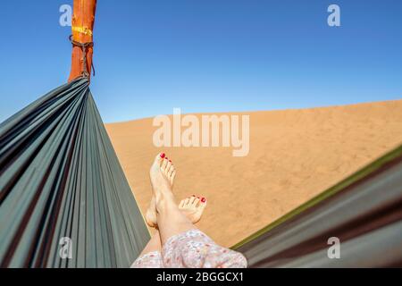 Young woman relaxing in green hammock with view on sand dunes of Sahara Desert, Morocco, Africa Stock Photo