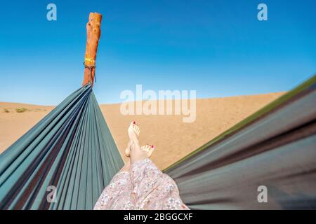 Young woman relaxing in green hammock with view on sand dunes of Sahara Desert, Morocco, Africa Stock Photo