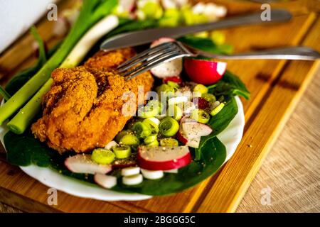 Fried meat in plate with spinach, radishes and spring garlic Stock Photo