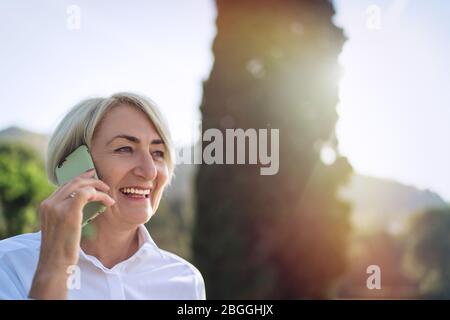 Smiling senior woman talking on mobile phone while resting at the park Stock Photo