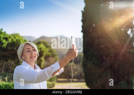 Smiling mature woman having a video chat through mobile phone while resting at the park Stock Photo