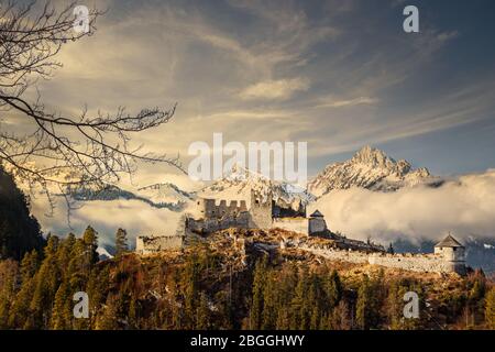 Snowy rocky mountains in clouds with medieval castle ruins and forest in the foreground