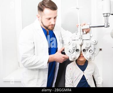 Optometrist doctor checks the young girl's eyesight. If the girl has poor eyesight, the doctor will give a prescription for glasses Stock Photo